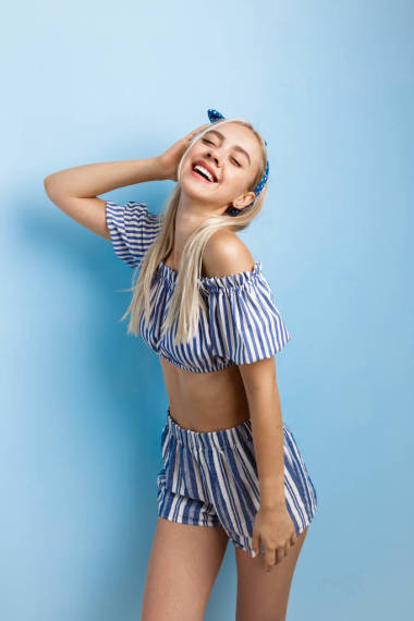 快乐而兴奋的美丽金发女孩穿着夏季服装, 摆姿势对着镜头, 站在蓝色的背景