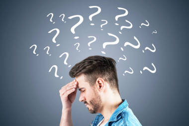 旁邊的景色是, 身穿牛仔褲襯衫的年輕人留著牛仔褲襯衫, 頭痛得厲害, 站在深灰色的墻上, 上面畫著問號。難題的概念