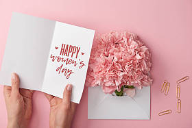 妇女拿着贺卡与愉快的妇女天的文字在康乃馨花附近的裁剪视图在信封在粉红色的背景