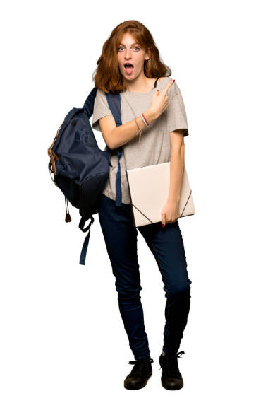 一個年輕的紅頭發(fā)的學生驚訝和指向的一面在孤立的白色背景的全長鏡頭