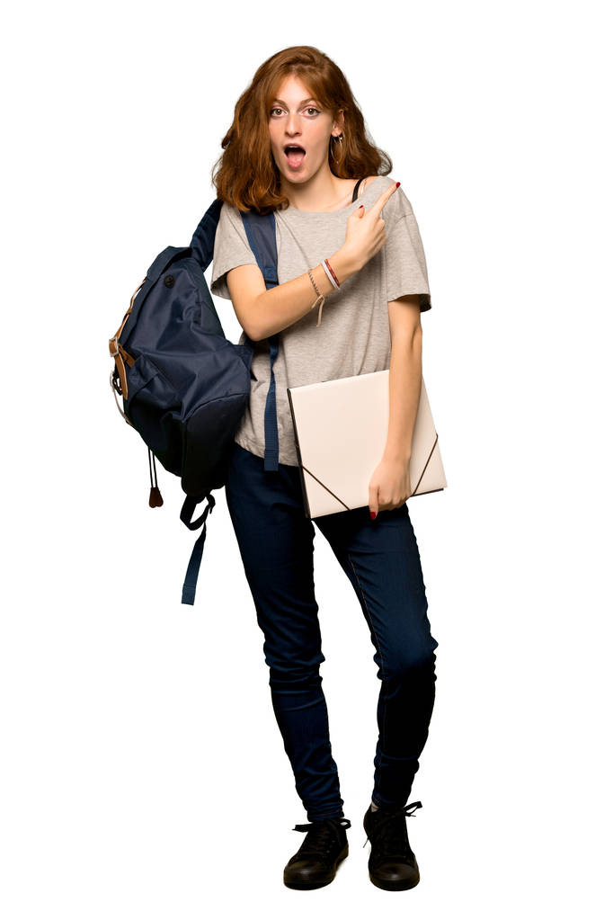 一个年轻的红头发的学生惊讶和指向的一面在孤立的白色背景的全长镜头