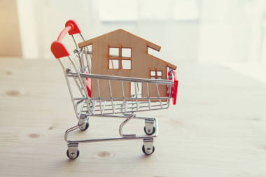 木制房屋模型在購物車, 房地產(chǎn), 買一個(gè)新的房子概念, 出售和租賃公寓, 新的房子為年輕的家庭