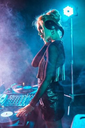美丽的 dj 女人与金发听音乐和举行耳机在夜总会与烟雾