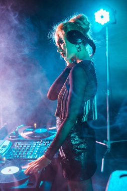 美丽的 dj 女人与金发听音乐和举行耳机在夜总会与烟雾