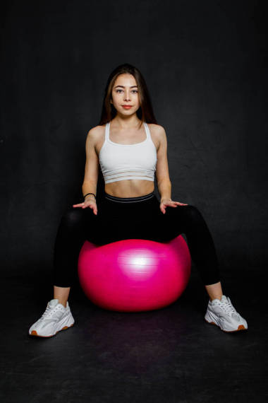 運(yùn)動(dòng)和強(qiáng)壯的年輕女子在黑色背景下的健身球上做一些鍛