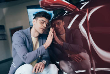 快樂時尚男子的選擇性焦點, 戴著眼鏡, 坐在紅色汽車附近, 閉著眼睛