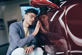 快乐时尚男子的选择性焦点, 戴着眼镜, 坐在红色汽车附近, 闭着眼睛