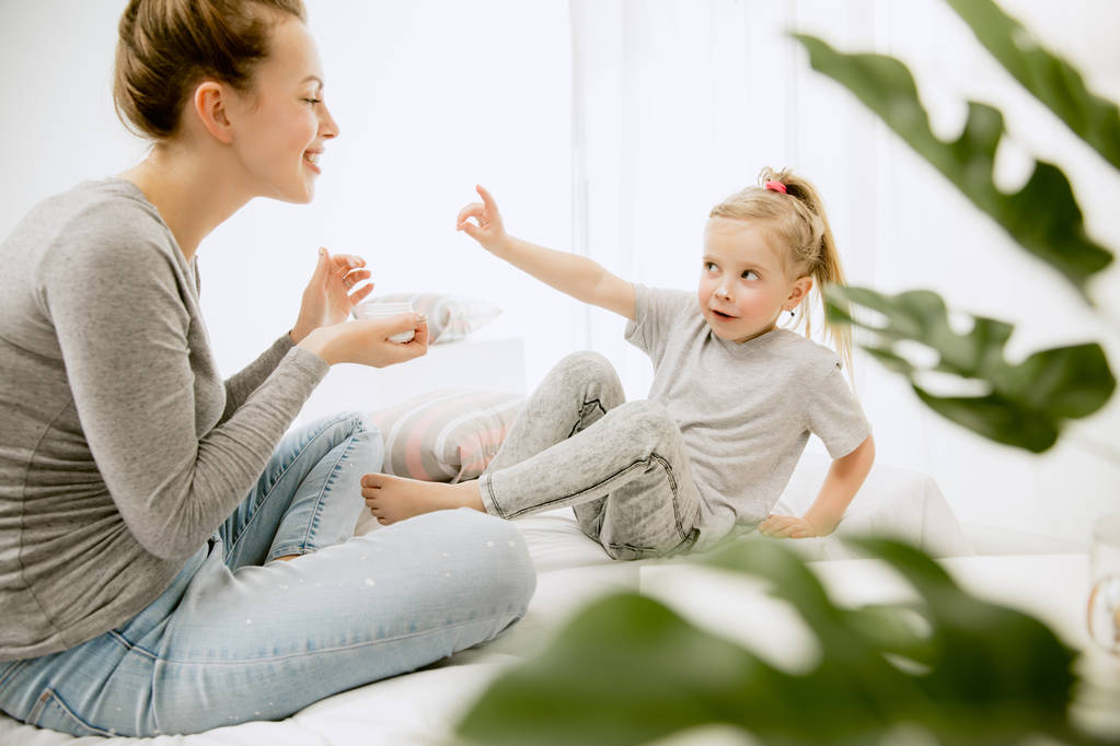 年轻的母亲和她的小女儿在床上拥抱和亲吻 年轻的母亲和她的小女儿在床上拥抱和亲吻