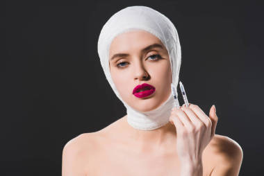 漂亮的年輕女子與包扎頭舉行注射器隔離在灰色 