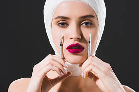 有吸引力的年轻女子与包扎头拿着注射器近脸隔离在灰色 