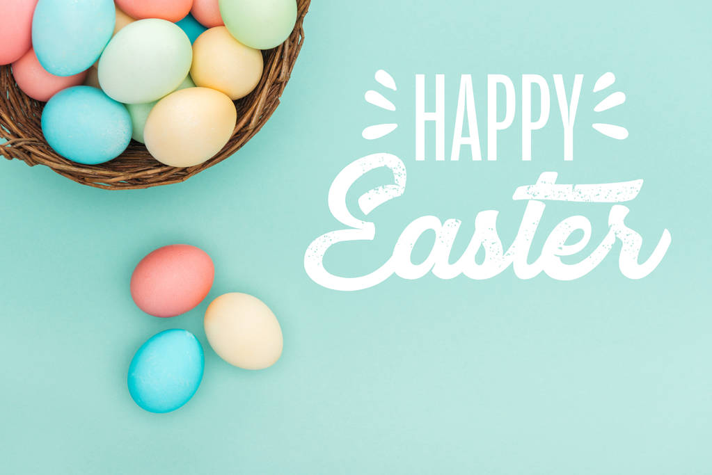 柳条篮中五颜六色的彩蛋的顶视图，蓝色背景上的白色快乐复活节字母