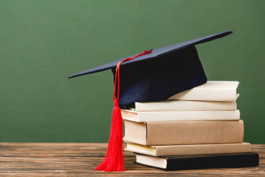 書籍和學(xué)術(shù)帽在木制表面隔離在綠色