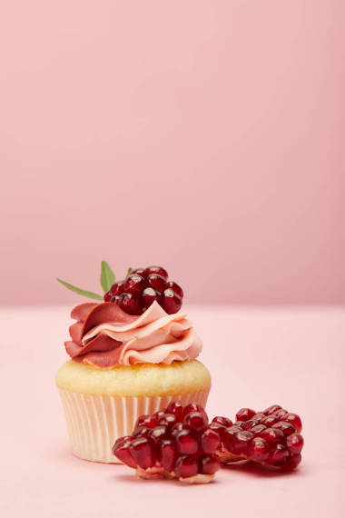 粉紅色表面上的甜紙蛋糕，奶油和石榴石