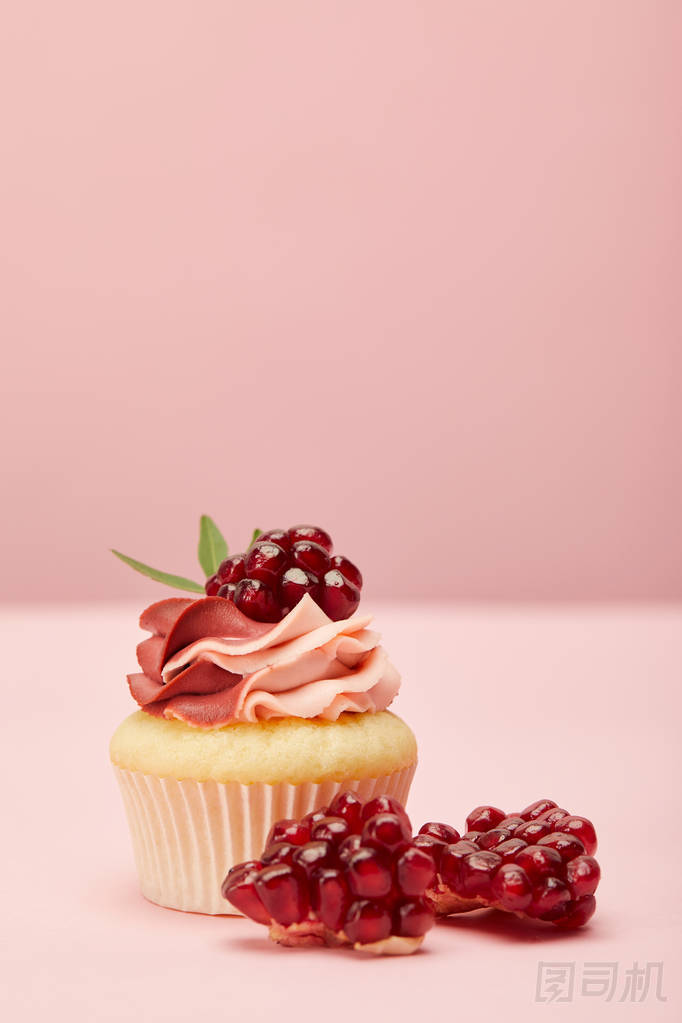粉紅色表面上的甜紙蛋糕，奶油和石榴石