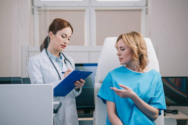 漂亮的醫(yī)生寫在剪貼板，而站在病人坐在扶手椅附近