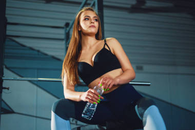 年轻迷人的运动女子坐在十字架上的水瓶上