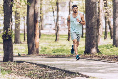 穿著運動服的帥哥在陽光明媚的公園里沿著人行道奔跑