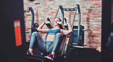 在健身房的訓練機里蹲下跑的女運動員。腿部肌肉訓練