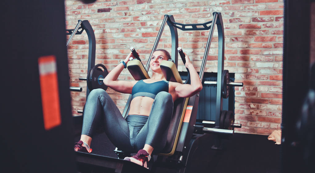 在健身房的训练机里蹲下跑的女运动员。腿部肌肉训练 在健身房的训练机里蹲下跑的女运动员。腿部肌肉训练