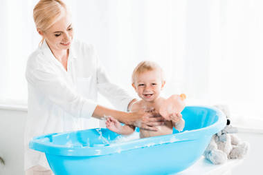 快樂的母親洗歡快的幼兒兒子拿著瓶子與洗發(fā)水 