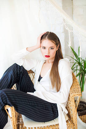 有吸引力的女孩模型与趋势化妆和长发休息在柳条柳条椅子旁边的吊床