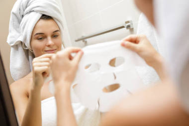 妇女在浴室是应用面部床单面具