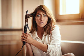  年轻的忧心忡忡的妇女卷曲头发与电动卷发器