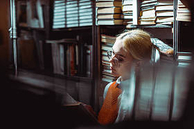 在图书馆中,美丽和金发女人阅读书籍的选择性焦点 