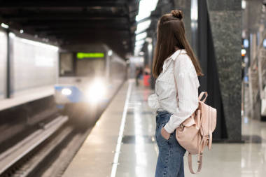 穿著牛仔褲和襯衫背著背包的年輕的歐洲姑娘在地鐵站等火車。 運動的背景模糊了傳達一種生機勃勃的氣氛. 這是一個快照的主意