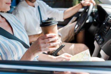 坐在車?yán)锏膵D女，拿著紙杯靠近司機(jī)的裁剪視圖 