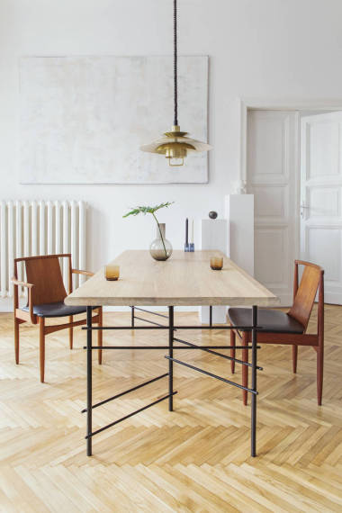 优雅典雅的用餐室内饰，配有设计共享桌、椅子、金色花灯、抽象绘画和时尚配饰。花瓶里的热带叶子。装饰独特。棕色木制镶木地板