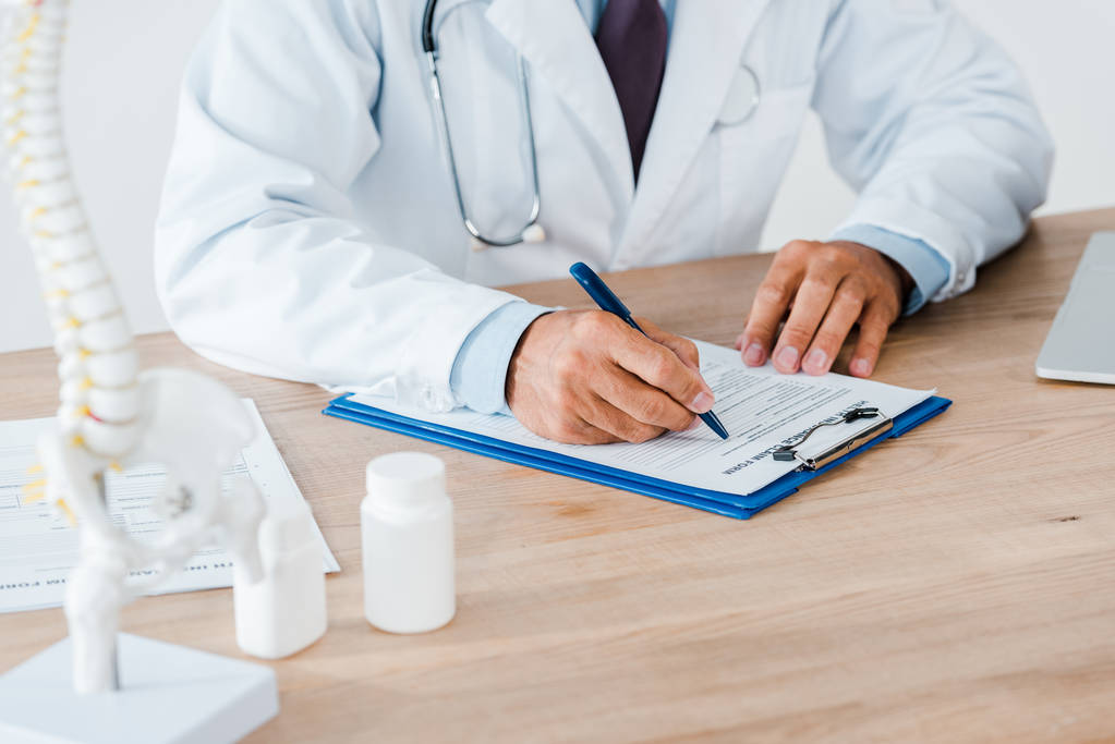 在医院用听诊器书写诊断的医生的裁剪视图  在医院用听诊器书写诊断的医生的裁剪视图