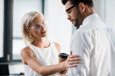 有吸引力的女人拿著紙杯和觸摸不安的同事在辦公室