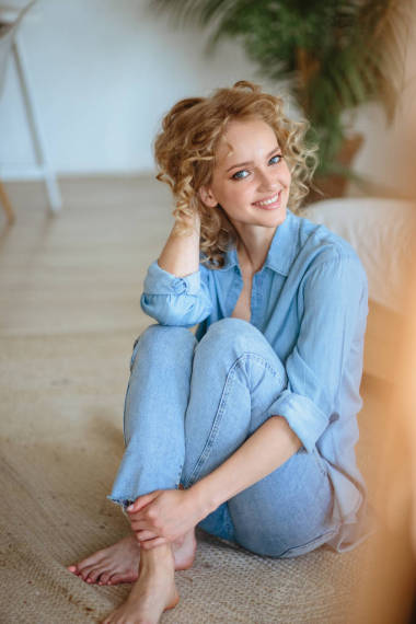 相当开朗的金发年轻女子卷曲的头发和迷人的微笑休息在她的家,房间与现代斯堪的纳维亚内部