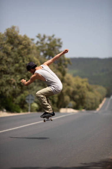 滑板手在街头服装服装表演跳魔术，而骑滑下道路在阳光明媚的日子