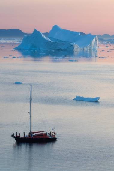 在極地夏季的午夜陽光季節(jié)，小紅帆船在迪斯科灣冰川漂浮的冰山之間巡航。伊盧利薩特，格陵蘭。南極海域冰山的考察船