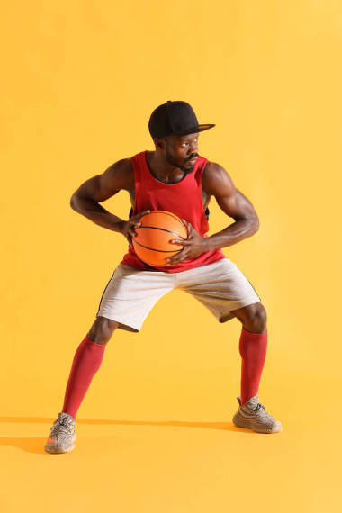 穿紅襯衫、黑帽和灰色短褲的黑人打籃球的全長肖像。工作室, 黃色背景