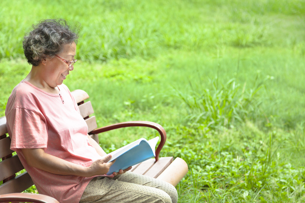 快乐的高级女人坐在长凳上,和读一本书 快乐的高级女人坐在长凳上,和读一本书