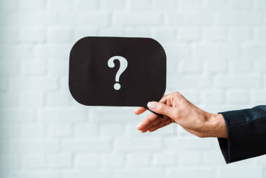 在白砖墙附近拿着黑色语音气泡与问号的妇女的裁剪视图 