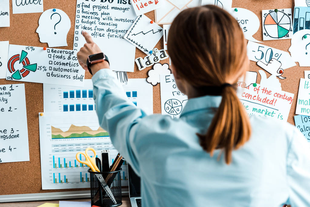 年轻女子用手指指着办公室内带有字母的告示牌的后视图 年轻女子用手指指着办公室内带有字母的告示牌的后视图