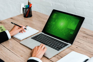 使用筆記本電腦時(shí)手持筆的裁剪視圖，屏幕上帶有圖表和圖形 