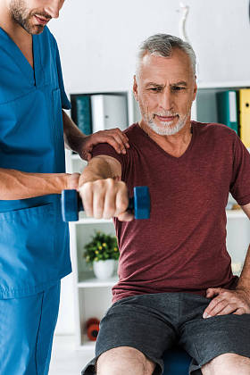 留着胡子的医生站在中年男子用哑铃锻炼的裁剪视图 