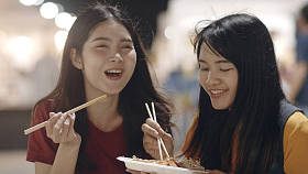 亚洲年轻女性朋友在泰国曼谷旅游，美丽的女性感觉快乐步行和吃垫泰在考三路。妇女旅游吃街头食品在泰国的概念