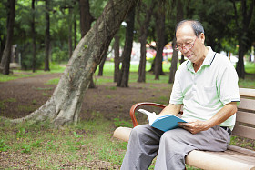 快乐的高级人坐在长凳上，读的书