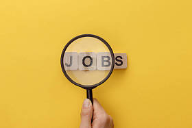 在纸板方块下拿着放大镜的妇女的裁剪视图，在黄色背景上用工作字母