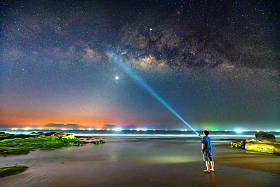 夜景与乳白色的方式和剪影的一个快乐的男人站在沙滩上的青苔岩石旁边