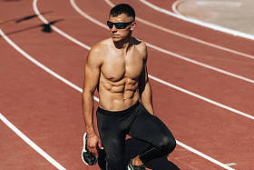 无衬衫的年轻运动员准备在体育场跑道上跑步的画面。运动员，男子短跑在训练中为比赛。人、运动和健康生活方式