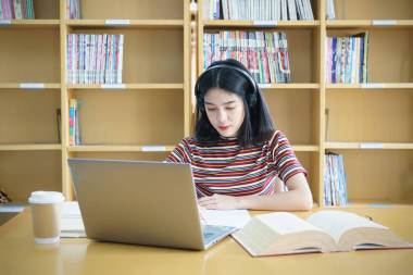 一個(gè)女大學(xué)生坐在桌旁做大學(xué)圖書(shū)館的作業(yè)。 學(xué)生使用筆記本電腦，在網(wǎng)上學(xué)習(xí)
