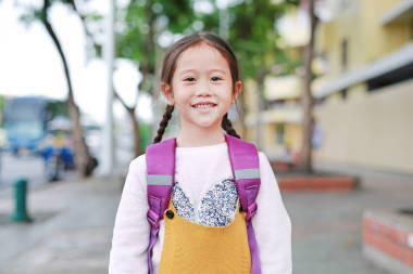 快樂的亞洲女孩行走與學(xué)生肩書包。小女生，有背包前視圖?；氐綄W(xué)校概念