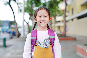 快乐的亚洲女孩行走与学生肩书包。小女生，有背包前视图。回到学校概念